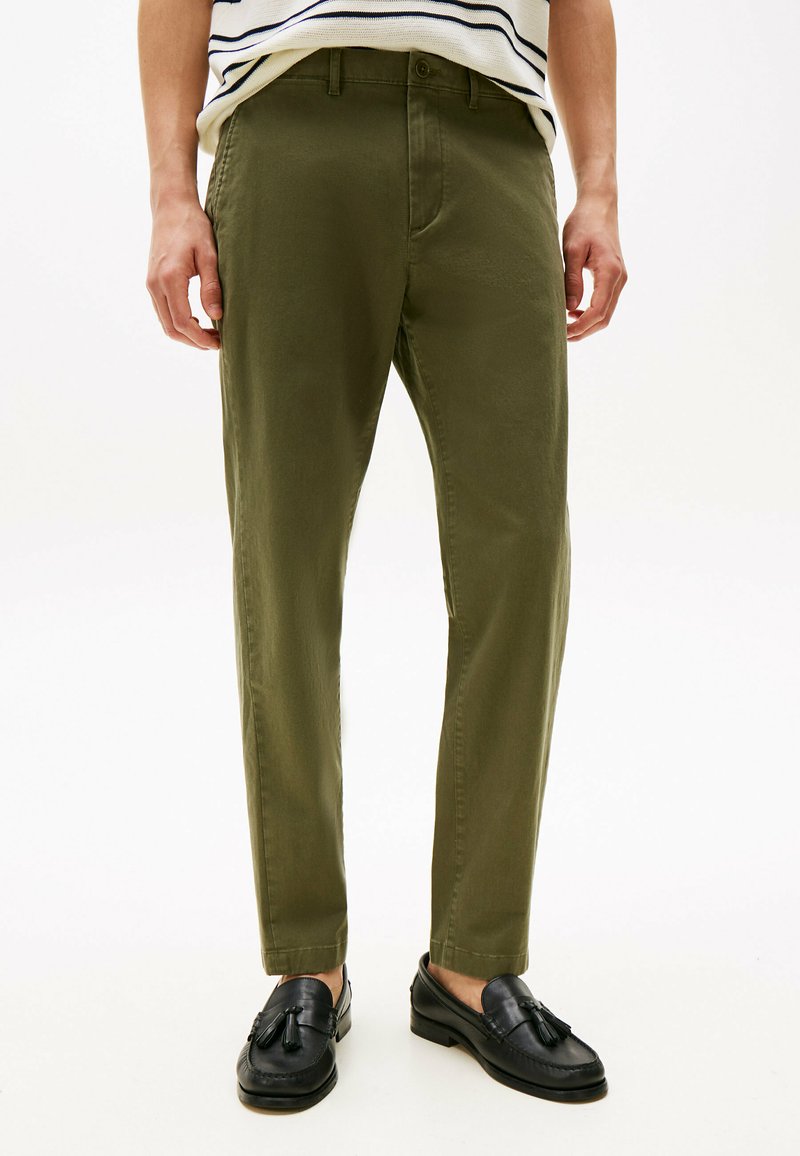 Pantaloni verde oliva con taglio dritto, realizzati in tessuto leggero, con tasche frontali e una texture liscia, abbinati a mocassini neri.