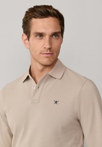 Polo beige en tissu texturé ; doté d'un col classique, d'une patte de boutonnage à trois boutons et d'un petit logo bleu marine sur la poitrine.