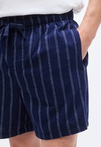 Σορτς σε ναυτικό ρίγες από απαλό ύφασμα, με κάθετες λευκές ρίγες, ελαστική μέση με κορδόνι και πλαϊνές τσέπες.