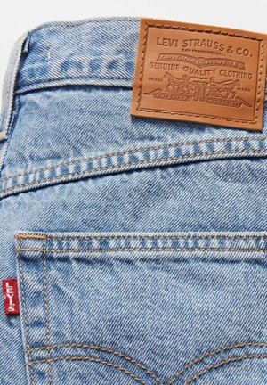 Vaqueros de mezclilla azul claro con un parche de cuero con logotipo en relieve, costuras naranjas y una etiqueta roja de Levi's cerca del bolsillo.
