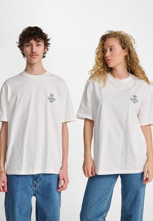 Hvide bomulds t-shirts med korte ærmer, der har et lille grønt grafisk logo på brystet. Sæt sammen med denimbukser.