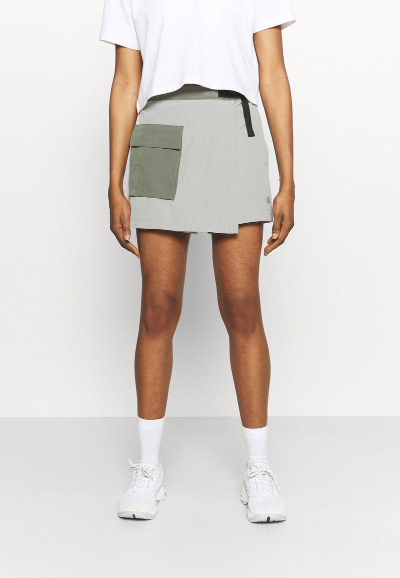 Falda verde claro con un diseño de envoltura, que cuenta con un gran bolsillo frontal. Hecha de material ligero, combinada con una camiseta corta blanca y zapatillas blancas.