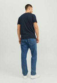 Tricou bleumarin cu mânecă scurtă, asortat cu blugi drepți de culoare albastru deschis și adidași albi, văzut din spate. Design simplu și croială confortabilă.