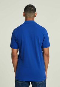 Polo a maniche corte in cotone misto blu vivace. Presenta un colletto classico, polsini a coste e un orlo dritto.