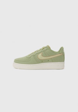 Low-top sneaker in light green fabric with beige Nike swoosh and white sole, shown from the outer side on a neutral background.