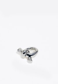 Anillo de metal plateado con una superficie lisa y pulida, que presenta un diseño abstracto con formas redondeadas y una estructura robusta.