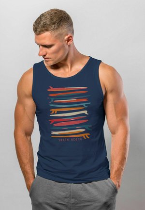 Navy Tanktop mit buntem, horizontalem Pinselstrichdesign und dem Schriftzug "SOUTH BEACH". Der Stoff wirkt weich; der enganliegende Schnitt betont die Figur.