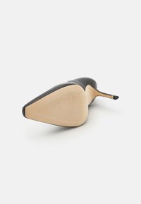Scarpa nera con tacco alto, punta affusolata, tomaia in pelle liscia e suola beige testurizzata, dotata di un sottile tacco stiletto.