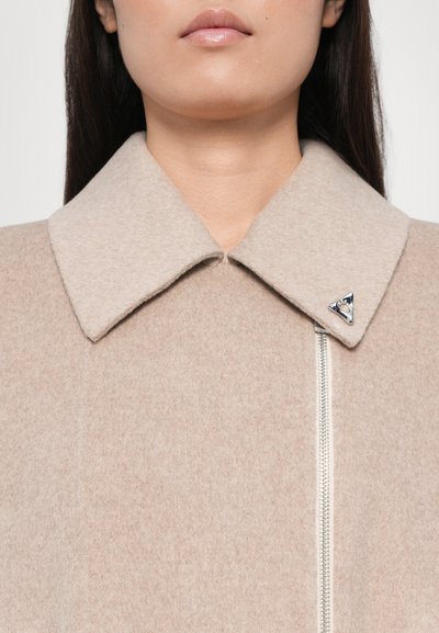 Beige wool coat with large collar, silver zipper, and triangular logo accent. Soft texture, clean design with minimal detailing.