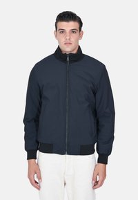 Giacca bomber navy con zip frontale, polsini e colletto a coste. Realizzata in tessuto morbido, con tasche laterali e un design aderente.
