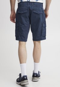 Shorts cargo de culoare albastru închis, cu buzunare laterale mari, material texturat și croială relaxată. Purtați cu șosete albe și adidași navy.