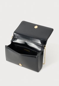 Borsa in finta pelle nera con finiture dorate. Presenta una tracolla a catena e una chiusura a scatto. L'interno ha un compartimento con il marchio visibile.