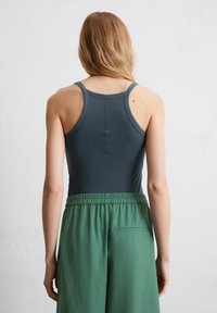 Top in cotone grigio scuro con scollo a barca, abbinato a pantaloni verdi larghi con cintura elastica e tasca laterale. Tessuto morbido.