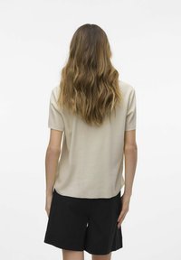 Top beige de manga corta con un corte relajado, presenta una textura suave y un dobladillo redondeado, combinado con pantalones cortos negros, visto desde atrás.