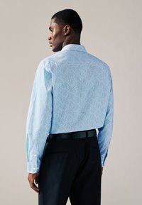 Ljusblå långärmad skjorta med blommönster i rött och vitt, med standardkrage och knäppning vid ärmslut, bärs tillsammans med svarta byxor.