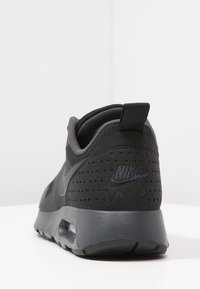 Svarta Nike Air Max-sneakers sedd bakifrån, med perforerat mocka, synlig luftsula och dragflik på en vit bakgrund.