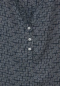 Camicia blu navy con un motivo geometrico bianco, caratterizzata da un collo a V e cinque bottoni bianchi lungo la patta frontale.