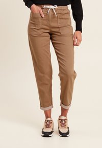 Lichtbruine katoenen cargobroek met een elastische tailleband en trekkoord. Bevat twee voorzakken en opgerolde manchetten.
