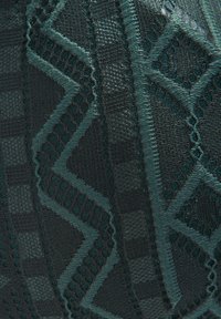 Donkerblauw groen gestippeld stof met geometrische vormen en texturen, waaronder kant, gaas en glanzende accenten in een zigzagpatroon.