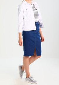 Vitt denimjacka, randig skjorta, blå blyertskjol med slits fram, och grå sneakers, mot en neutral bakgrund.