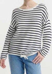 Sweter w paski w kolorze kremowym i granatowym, charakteryzujący się luźnym krojem, szerokim dekoltem i wiązaniem na dole. Tworzywo o teksturowanym dzianinie.