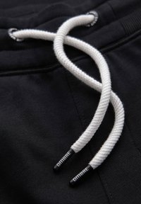 Svarta joggers i tyg med vita snören. Snörena har svarta spetsar med texten "DIMBRE." Slät textur, avslappnad design.