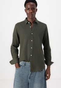Mörkgrön linneskjorta med button-down krage, långa ärmar och vita knappar, ihopparad med ljusblå denimshorts.