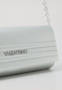 Hellblaue Lederhandtasche mit Klappenverschluss, vertikalen Rippendetails und silberner Kettenriemen. Graviertes "VALENTINO"-Logo in Silber.