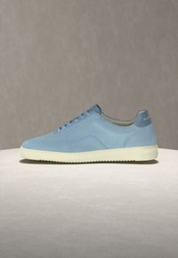 Ανοιχτό μπλε χαμηλό αθλητικό παπούτσι με κορδόνια και λευκή σόλα σε επίπεδη ουδέτερη επιφάνεια και γκρίζο φόντο.