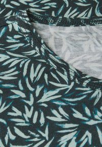 Tela negra con un patrón de hojas en azul claro y verde azulado. Textura suave, con cuello redondo y costuras reforzadas en los bordes.