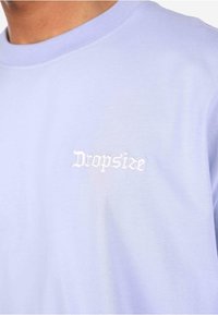 Lys lilla bomull T-skjorte med rund hals og korte ermer, med hvit brodert "Dropsize" tekst på brystet.