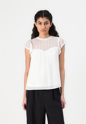 Blusa blanca con un panel de encaje texturizado en la parte superior, mangas cortas con volantes y un cuerpo inferior liso. Cuello redondo, ajuste fluido.