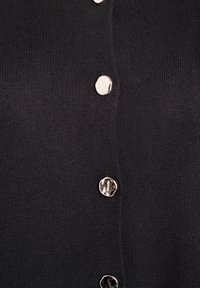 Close-up van donker geribbeld stof met vier glanzende, onregelmatige zilveren knopen die verticaal zijn uitgelijnd.