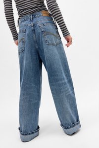Bredde denim jeans i blått med rullekanter, med to baklommer og et brunt lærmerke i midjen. Forsterket søm-detalj.