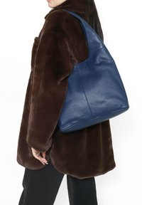 Borsa a mano in pelle blu con una texture morbida, design hobo e base arrotondata. La borsa presenta una tracolla regolabile per un trasporto facile.