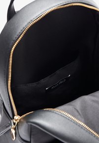 Svart syntetisk ryggsäck med en guldzipper, som har ett rymligt inre och en märkt svart tygficka. Slät textur genom hela väskan.