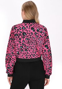 Tætsiddende bomberjakke med et klart pink stof, der har sorte og blå leopardpletter, elastiske ærmer og en sort krave.