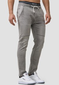 Pantalones jogger de denim gris con cinturilla elástica, cordón y bolsillos laterales. La tela presenta una textura suave y sutiles detalles de costura.