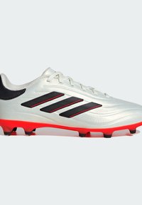 Crampons de football argentés avec accents noirs et semelle rouge. Dotés d'un design élégant, d'une surface texturée et de trois rayures noires sur le côté.