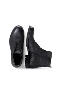 Twee paar zwarte leren schoenen: een is een stijlvolle enkelboot met een rits, de ander is een klassiek veterschoen, tentoongesteld tegen een witte achtergrond.