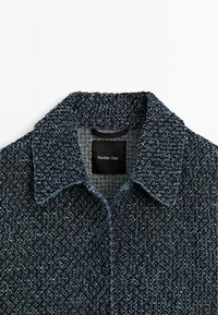 Dark blue textured jacket with a collar, featuring a black label that reads "Massimo Dutti." The background is plain white.