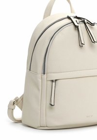 Petit sac à dos en cuir couleur crème avec deux compartiments zippés, garniture noire sur les tirettes des fermetures éclair et bretelles réglables.