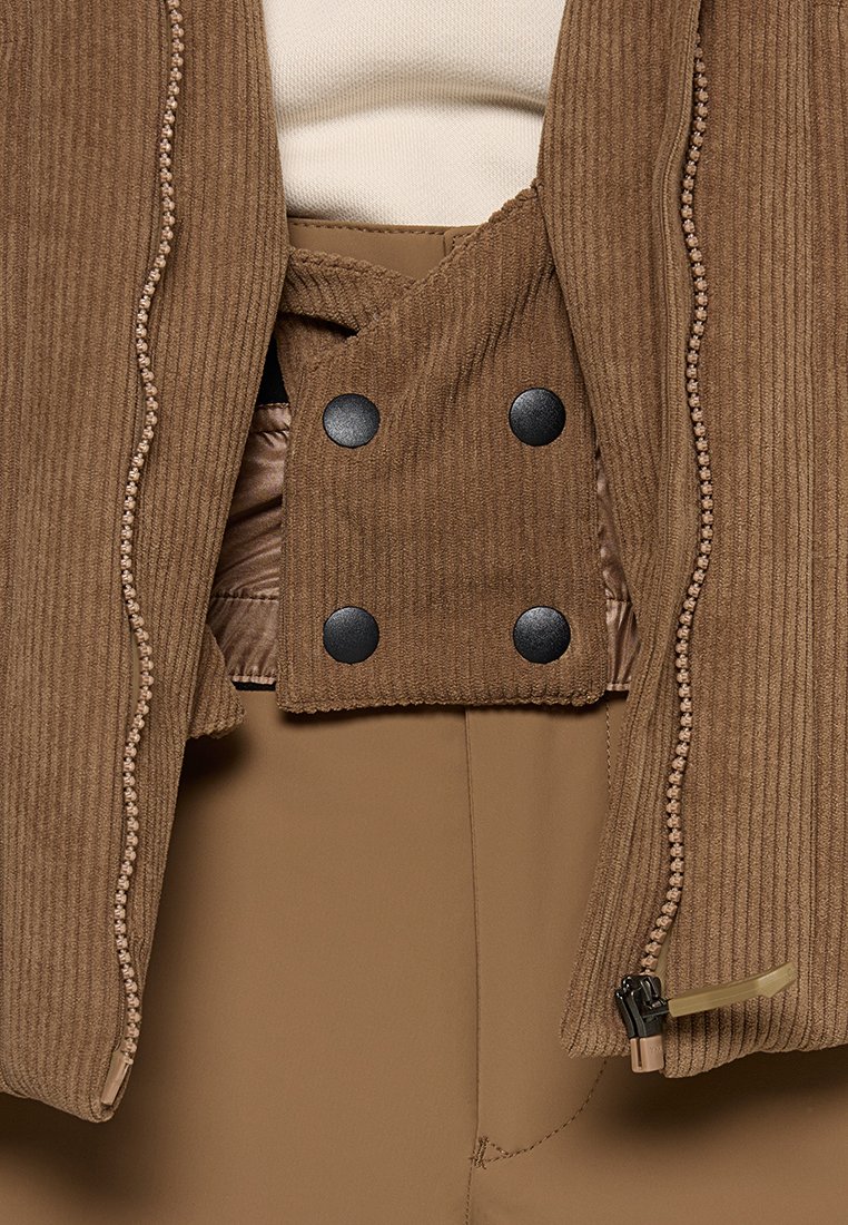 Braune Cordjacke mit einem gesteppten Innenfutter, ausgestattet mit schwarzen Druckknöpfen und kontrastierenden Nähten. Reißverschlussdetails am Saum sichtbar.