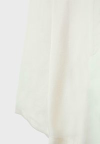 Gros plan de la partie inférieure d’un vêtement en tissu blanc avec une couture subtile et une texture douce visible.