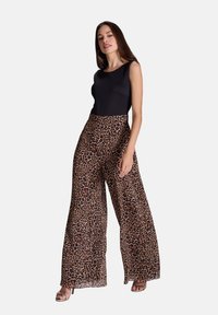 Bodysuit sans manches noir associé à des pantalons larges en imprimé léopard. Les pantalons présentent une texture fluide et légère avec un design taille haute.