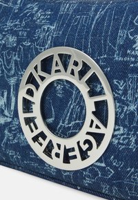 Borsa in denim blu con motivi grafici bianchi, caratterizzata da un accento circolare in argento con lettere intagliate. Finitura testurizzata, forma rettangolare.