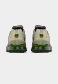 Αθλητικά παπούτσια Nike Air Max με γκρι πλέγμα στο πάνω μέρος, πράσινες λεπτομέρειες και διαφανή αερόσολα στη φτέρνα. Υφή με ανάγλυφα μοτίβα στα πλαϊνά.