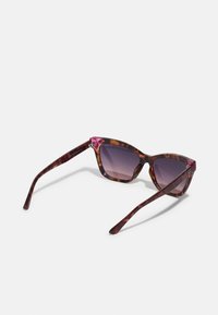 Lunettes de soleil en écaille de tortue avec un design cat-eye audacieux, des détails d'accent rose et des verres sombres dégradés. Comprend des branches fines pour une sensation légère.