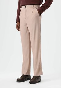 Beige geplooide broek met verticale strepen, voorzien van een rechte pijp, steekzakken aan de voorkant en een knoopsluiting. Geweven stof.