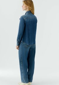 Jeanshemd mit figurbetonter Silhouette, Farbverlauf von Hell- bis Dunkelblau, lange Ärmel und Knopfdetails an den Manschetten, kombiniert mit passenden Jeanshosen.
